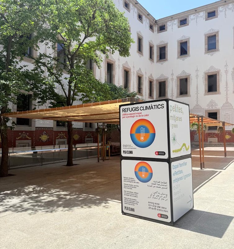 Foto mostra um edifício ao fundo; em primeiro plano, uma praça com toldos para sombra e um grande bloco escrito